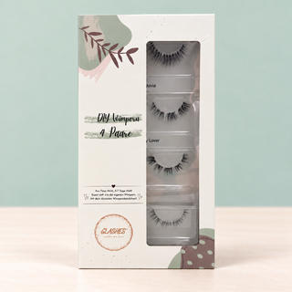 Stehende Glashes All Day Box mit Sichtfenster und vier DIY-Wimpernpaaren vor salbeigrünem Hintergrund
